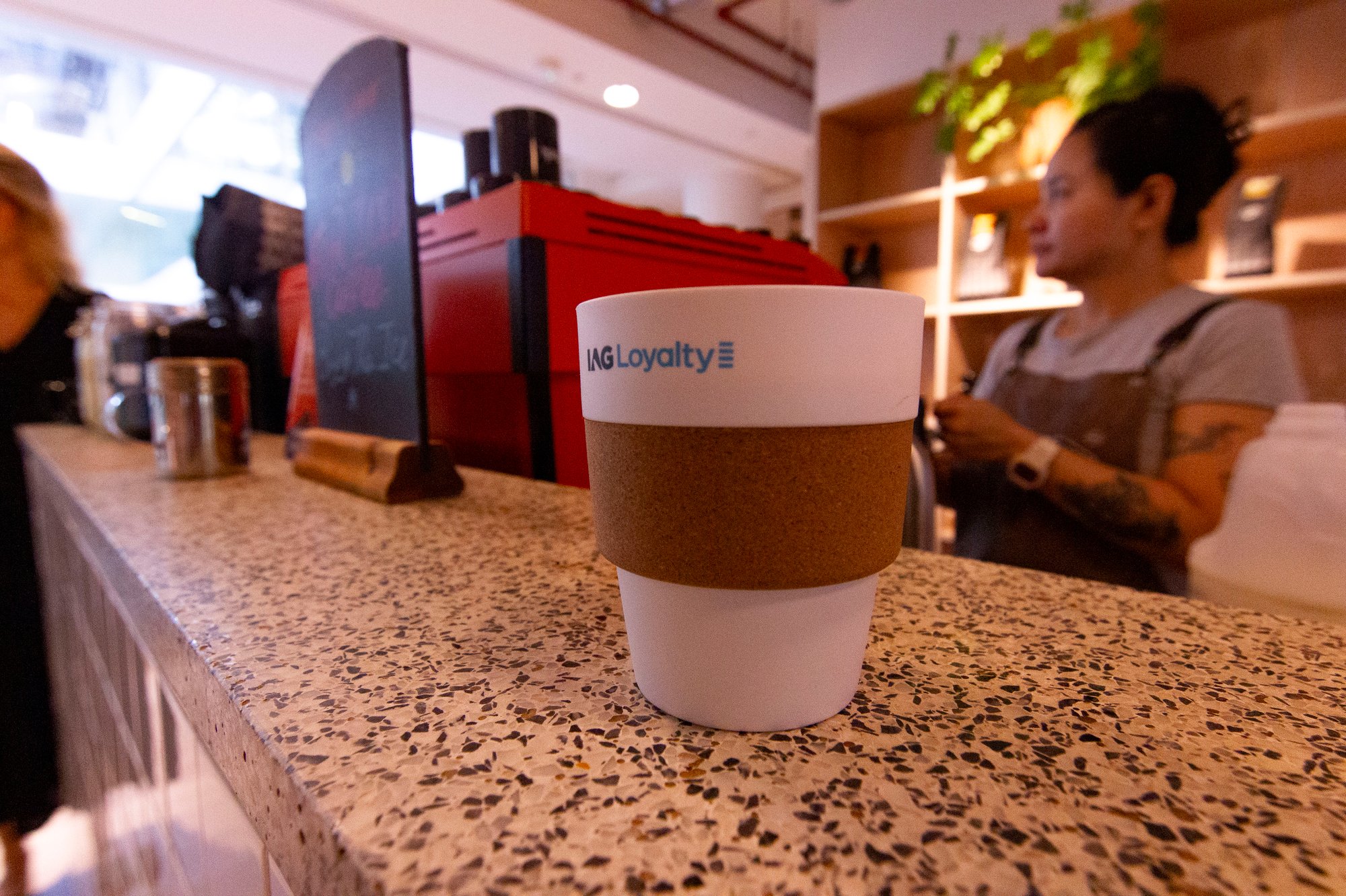 Cup of coffee on a bar with branding IAG Loyalty on the cup Cup of coffee on a bar with branding IAG Loyalty on the cup